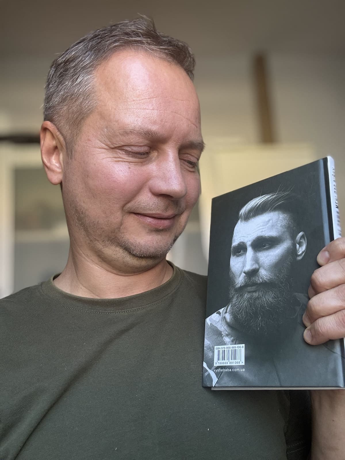 Andrej Slabinsky holding the second edition of «Тільки не пиши мені про війну», back cover with the ISBN barcode and vyshebaba.com.ua towards the camera